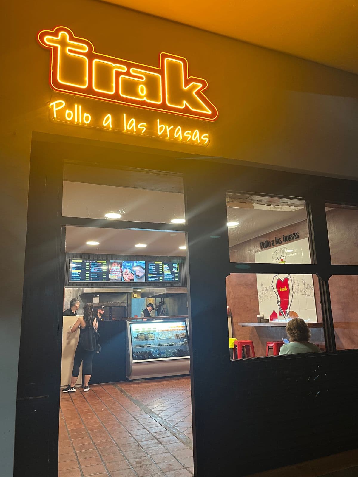Fachada de un local de Pollo Trak con el rótulo iluminado